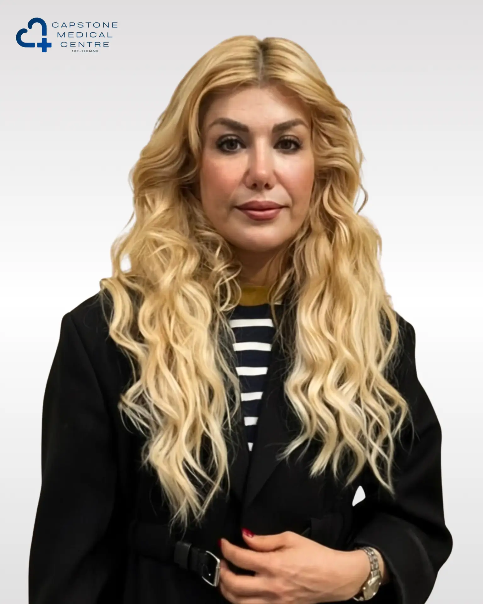 Dr.Maya - Capstone Medical Centre Southbank - Capstone Medical Centre Southbank Portrait of a blonde woman in a black blazer and striped top with a Capstone Medical Centre logo in the top-left corner.